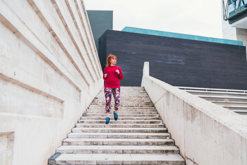 General shot from behind of a sporty red-haired caucasian female running up stairs outdoor