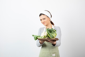 Photo of a young woman in apron holding a wooden plate with cauliflowers