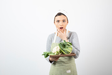 Photo of a young woman in apron holding a wooden plate with cauliflowers