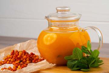 Glass teapot with . sea ​​buckthorn on wooden table
