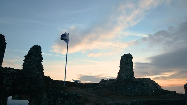 Flag of small town Kamnik waving in light breeze on top of ruins of old castle. Middle ages ruins. Beautiful lights of sunset in Slovenia. Static shot, real time
