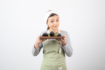 Photo of young female cook holding plate of eggplants on white background