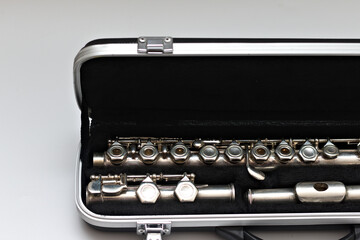Partial view of shiny disassembled silver flute in black case against white background