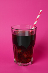 Glass of cola with ice cubes and straw on pink background