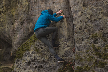 man in a blue jacket climbing a stone wall holding with strong hands in a crack in the stone wall
