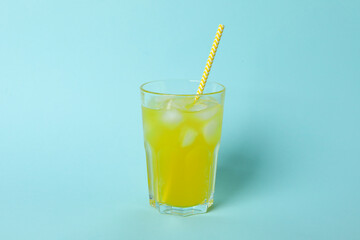 Glass of orange soda with ice cubes and straw on blue background