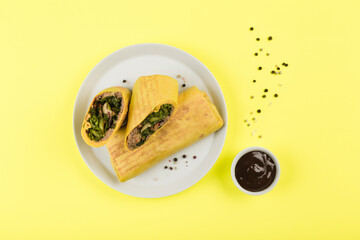 Burrito with meat in a flatbread on a bright yellow background with barbecue sauce.