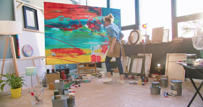 Caucasian young talented excited female contemporary painter working in art studio creating masterpiece on big canva. Woman artist drawing painting in own workshop. Contemporary art, rear concept