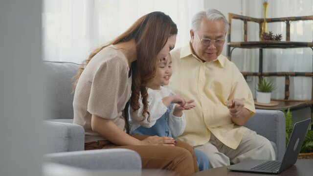 Happy family senior grandfather, daughter and granddaughter talking online via video chat using laptop computer with father, old grandpa embracing little grand child and mother in living room at home