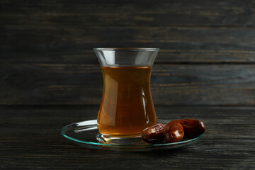 Saucer with glass of tea and dates on wooden background