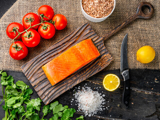 Cold smoked trout fillet with tomatoes and a knife on wooden cutting board. Closeup of a whole piece