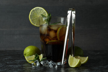 Glass of Cuba Libre and ingredients on dark background