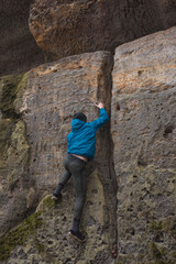 man in a blue jacket climbing a stone wall holding with strong hands in a crack in the stone wall