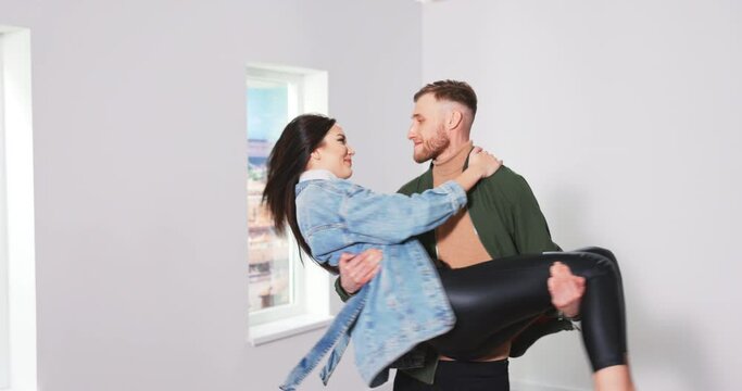 Excited happy couple first time home owners renters celebrate moving day in new flat concept, husband lifting young wife among boxes relocating into own house enjoy family goals achievement concept