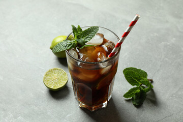 Glass of Cuba Libre and ingredients on gray background