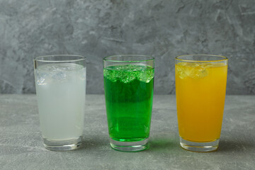 Glasses of different soda on gray background