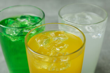 Glasses of different soda on gray background, close up