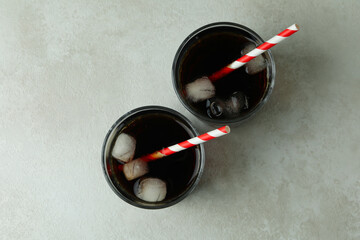 Glasses of cola with ice cubes and straw on white textured background