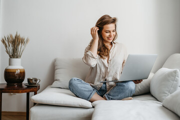 Portrait of a young female freelancer sitting on the couch and using laptop at home happily