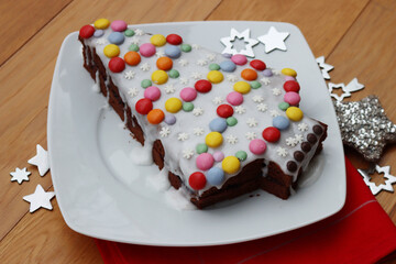 Chocolate cake in shape of a Christmas tree with white sugar glaze and colorful candies on a plate on wooden table