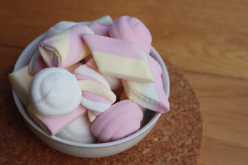 Colorful pink, white and yellow marshmallows in a bowl on wooden table