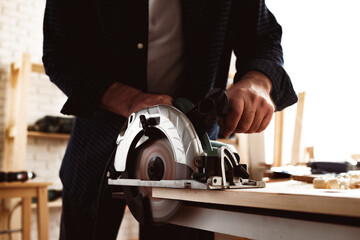 Fototapeta na wymiar Carpenter hands cutting wood with electrical saw