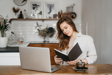 Young woman takes notes in front of laptop at home. Working from home. Concept of education and communication.