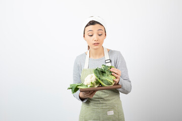 Photo of a young woman in apron holding a wooden plate with cauliflowers