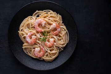 Pasta with shrimps on a black plate on a dark background