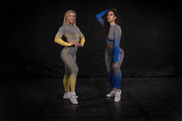 Fototapeta na wymiar two athletic girls with a confident look posing against a dark background, dressed in bright clothes for fitness