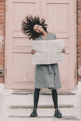 
A woman of model African American appearance holds a newspaper in her hands against the background of a brick building and waves her hair