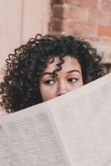 A woman of model African American appearance sits on a staircase and holds a newspaper in her hands against the background of a brick building