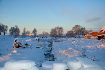 It's wintertime, snow covering field near village. Morning view with sun rays on the snow.