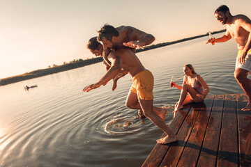 Young friends having fun enjoying a summer day swimming and jumping at the lake.
