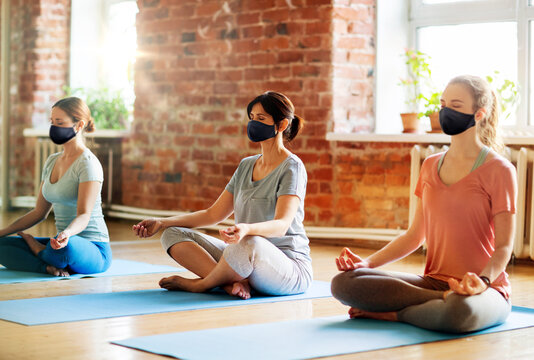 fitness, people and healthy lifestyle concept - group of women wearing face protective black masks for protection from virus disease meditating in lotus pose at yoga studio