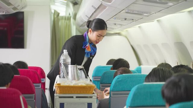 Asian flight attendant serving food or snack to passengers on airplane
