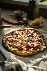 Homemade wholegrain pizza with cheddar cheese, mushrooms and tomatoes on baking paper on round kitchen table.