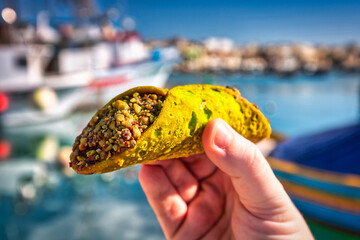 Maltese pistachio cannoli in hand at the fishing port of Marsaxlokk