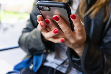 Caucasian woman with painted nails uses her mobile phone in a close-up with bokeh.