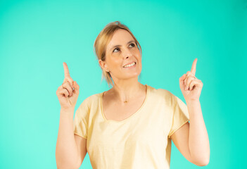 Portrait of a young woman dressed in casual t-shirt pointing fingers up at copy space isolated over green background