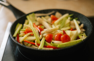 Cooking in the kitchen at home in a pan of fresh vegetables cut into strips: cherry tomato, zucchini, red pepper, eggplant