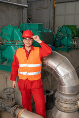 Young Technician in Red Coveralls and Hardhat Standing in Industrial Interior With Pipes and Generators
