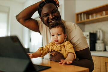 Beautiful baby sitting in the lap of her dad and looking at digital tablet, portrait.