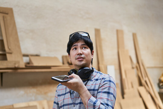 Craftsman apprentice using smartphone in carpentry shop