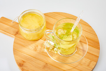 Transparent glass cup of herbal tea with linden flowers with honey jar on a  wooden board