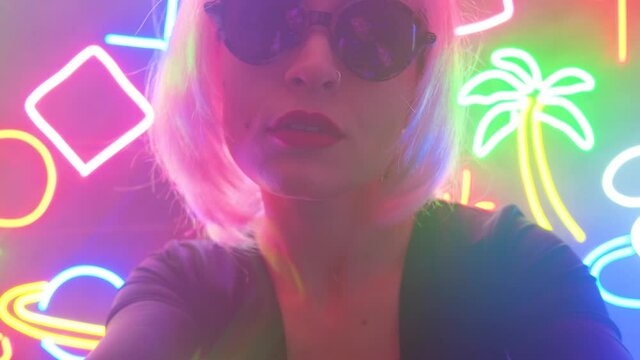 A girl in a pink wig and stylish glasses in neon light is dancing.