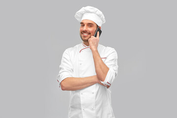 cooking, culinary and people concept - happy smiling male chef in toque and jacket calling on smartphone over grey background