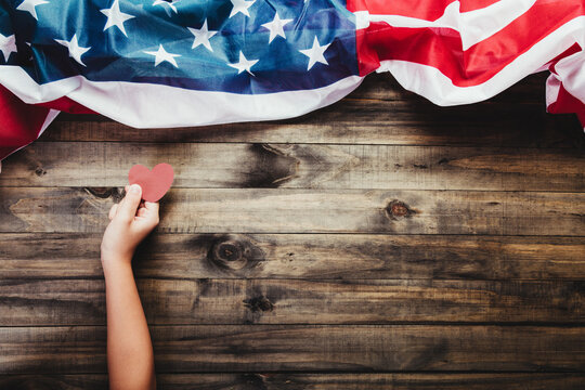 Young girl holding red heart cards in hands on American flag background. Love and patriotism for the country.