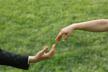 Close-up blurred female and male fingers touching each other in front of grass ground background