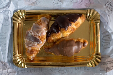 chocolate and sugar covered croissants on a golden tray. butter and saturated fat pastries. French gastronomy.